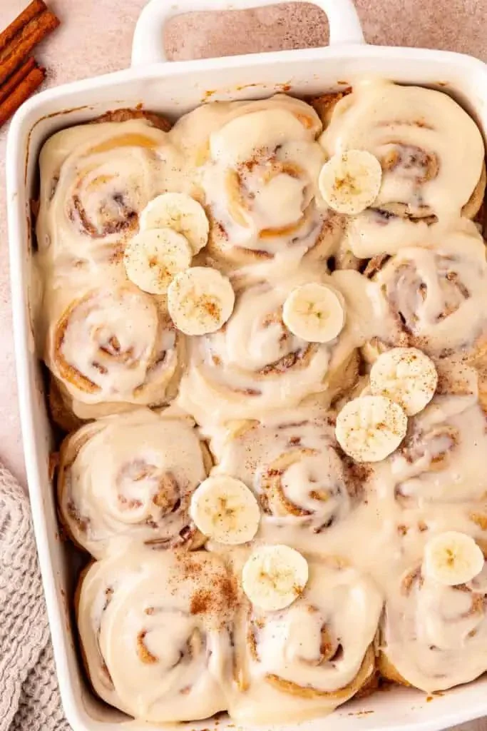Homemade banana bread cinnamon rolls topped with icing and banana slices.