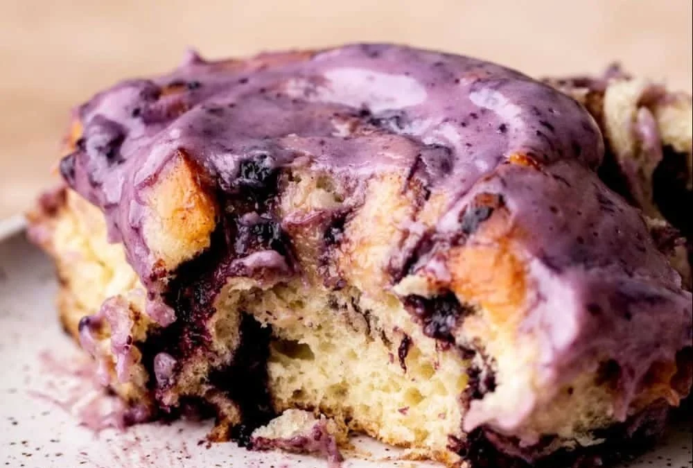 Freshly baked blueberry cinnamon rolls topped with glaze on a wooden table