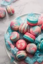 A plate of colorful cotton candy macarons with pastel colors and whimsical designs.