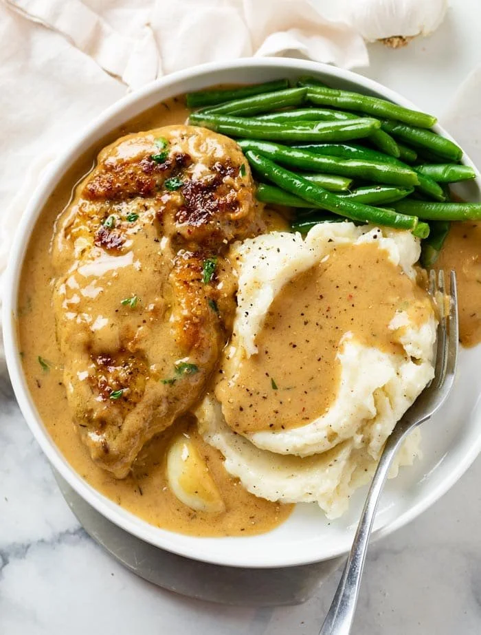 Delicious creamy garlic chicken plated with herbs and garlic cloves