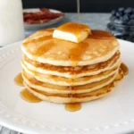 Fluffy pancakes stacked on a plate with syrup and berries