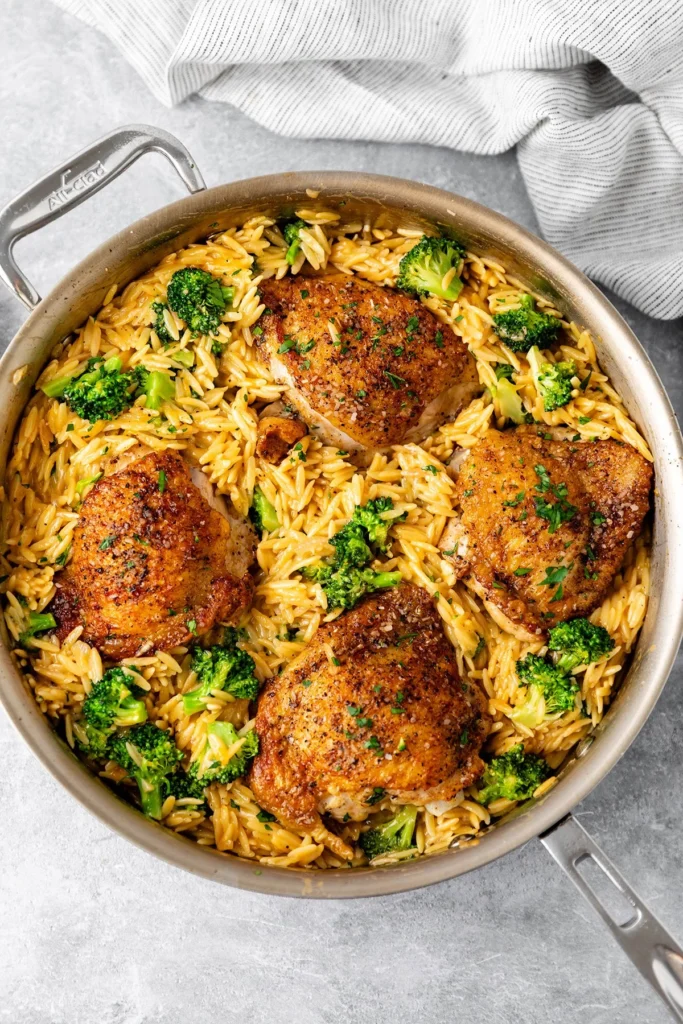 Skillet chicken thighs served with broccoli cheddar orzo in a pan