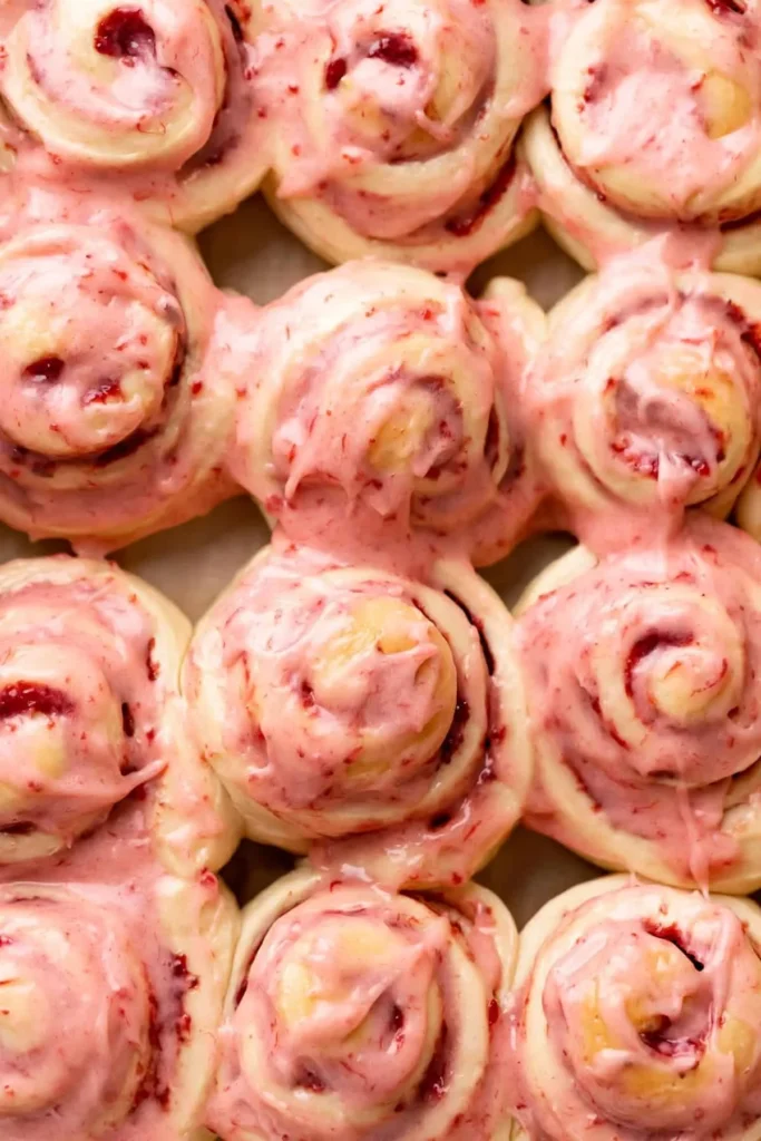 Freshly baked Strawberry Cinnamon Rolls drizzled with icing on a white plate.