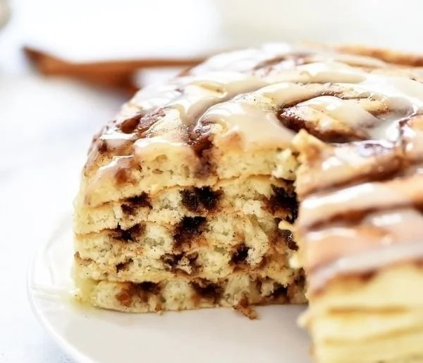 Fluffy cinnamon roll pancakes drizzled with icing on a white plate