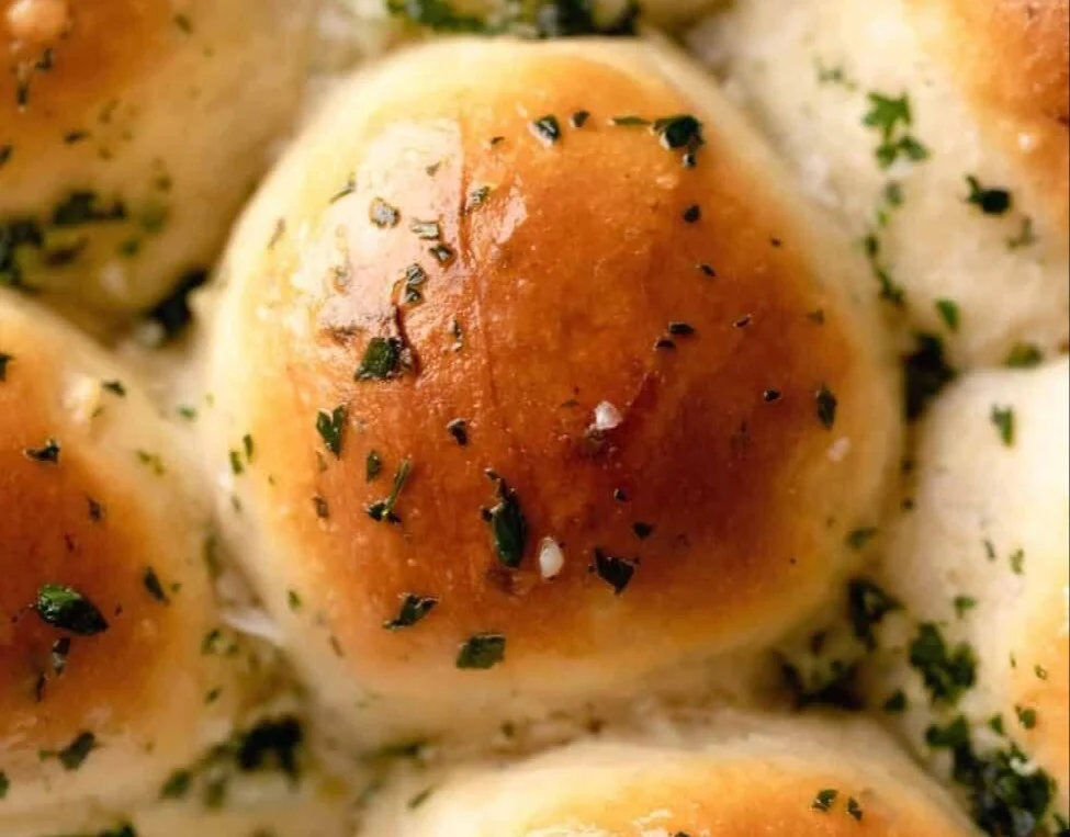 Freshly baked garlic butter bread rolls on a rustic wooden table.