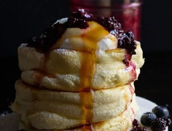 Fluffy Japanese souffle pancakes stacked on a plate with syrup and fruit.