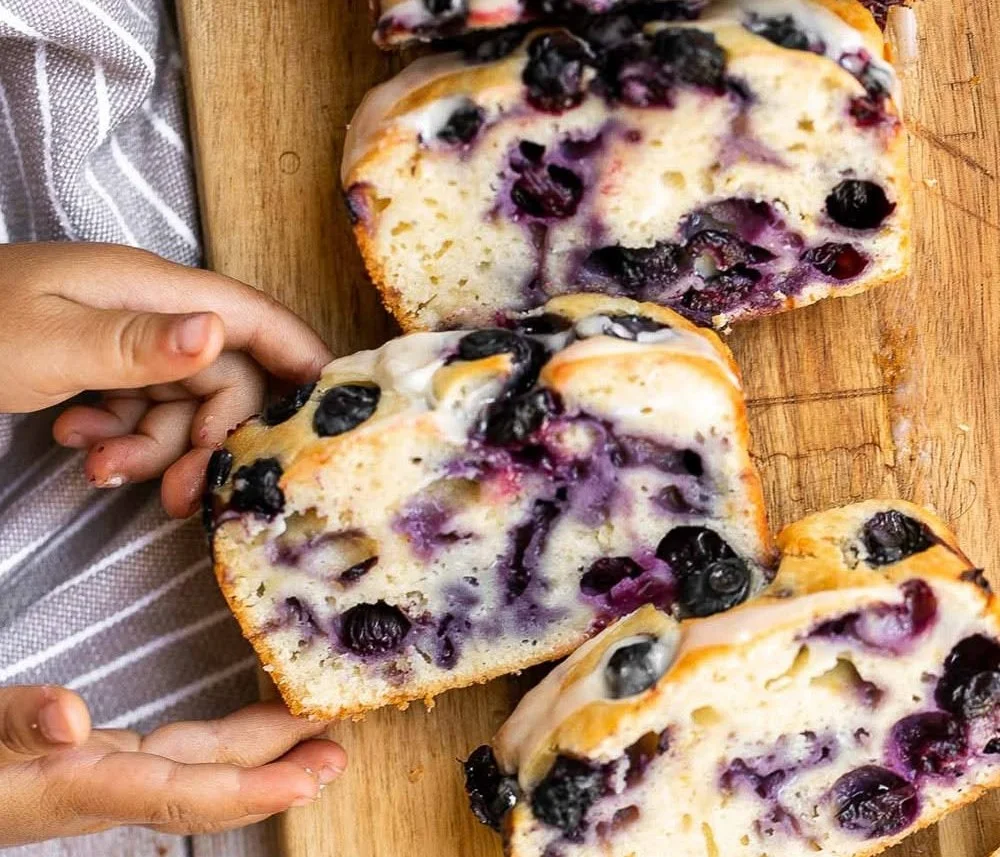 Loaf of lemon blueberry bread with blueberries and lemon slices on a wooden table