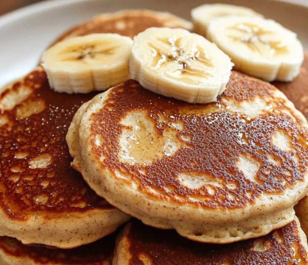 Delicious banana oatmeal pancakes stacked on a plate with syrup and banana slices