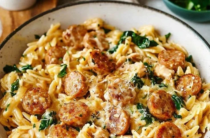 A creamy chicken sausage orzo dish garnished with herbs in a bowl.