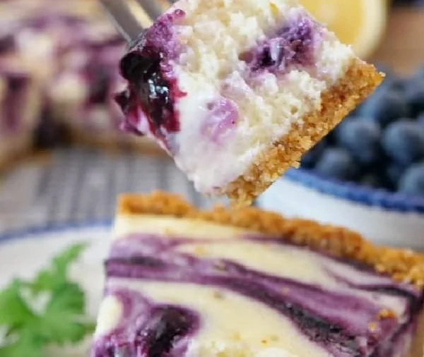 Slice of lemon blueberry cheesecake on a plate with fresh blueberries