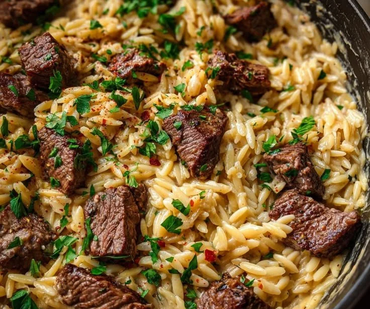 One pot creamy garlic butter steak orzo dish topped with fresh herbs, perfect for comfort food.