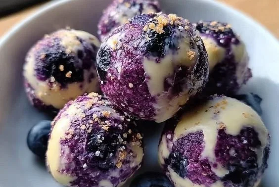 Blueberry cheesecake protein bites on a plate with fresh blueberries