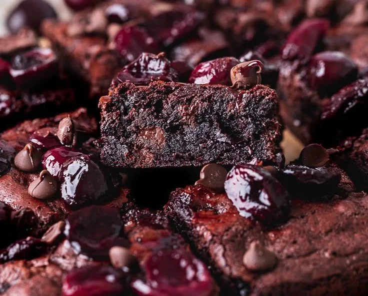 Delicious chocolate cherry brownies topped with fresh cherries on a wooden table.