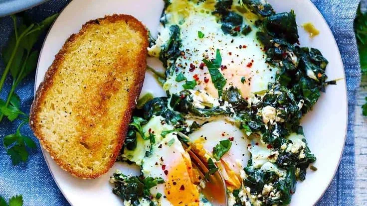 Creamy spinach dish with eggs served in a bowl, garnished with herbs.