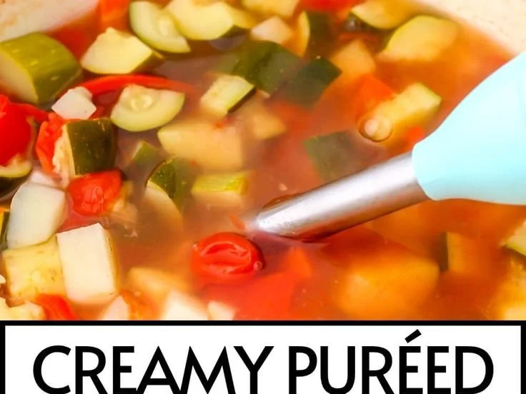 Bowl of creamy vegetable soup topped with fresh herbs and colorful vegetables.
