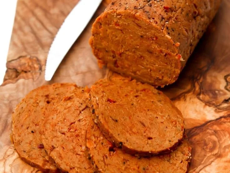 Homemade spicy vegan salami on a wooden board with fresh herbs.