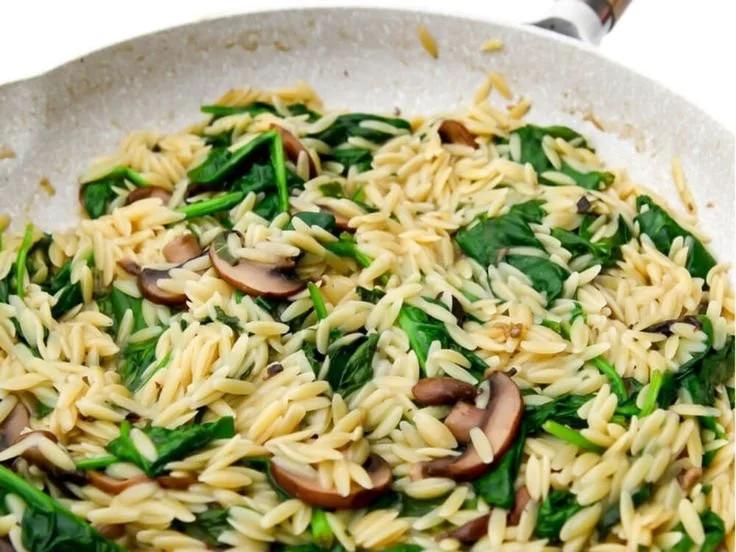 Bowl of creamy plant-based orzo risotto garnished with fresh herbs