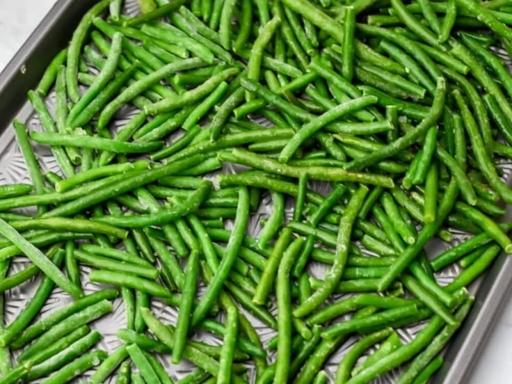 Deliciously roasted green beans served on a white plate with seasoning.