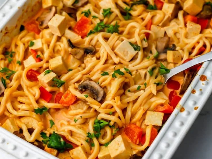 Bowl of Vegan Thai Red Curry Noodles with Tofu garnished with fresh herbs.